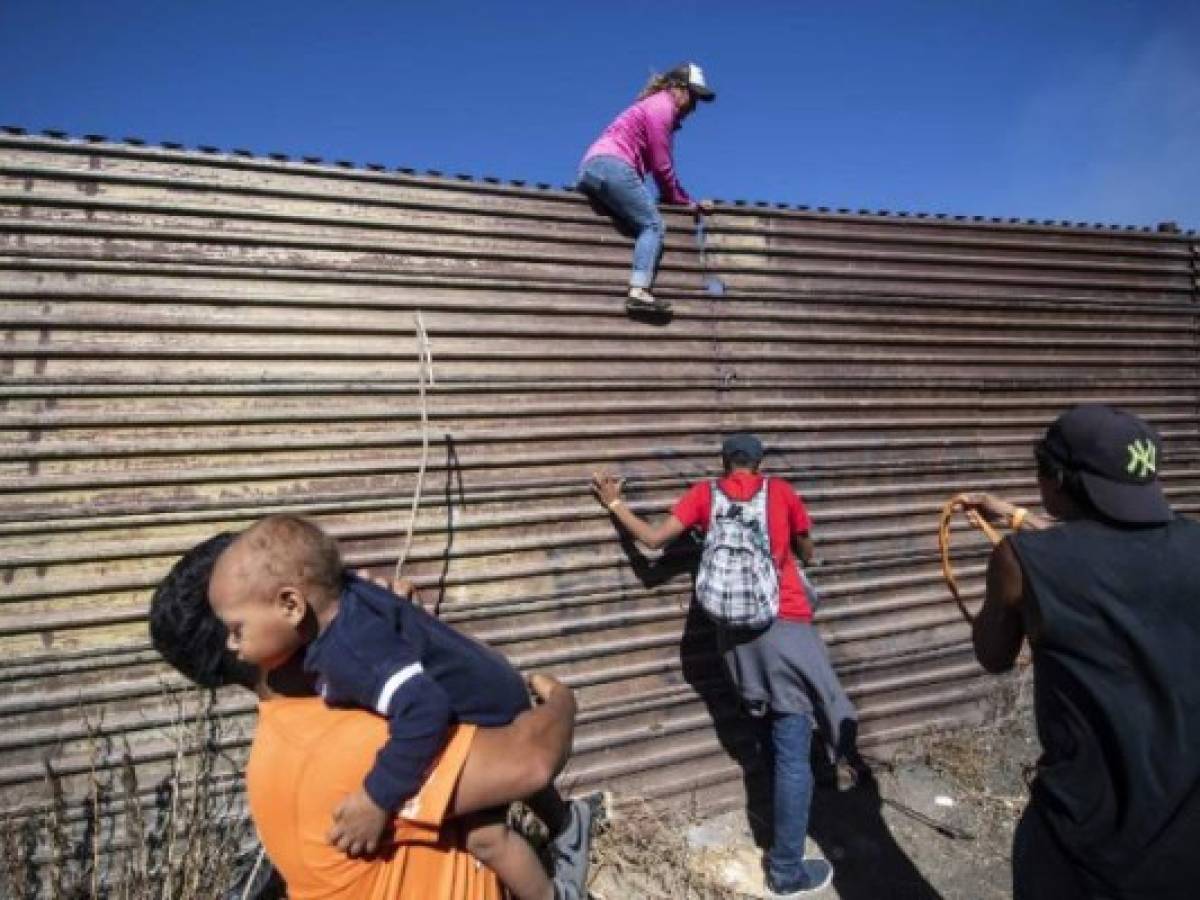 A group of Central American migrants -mostly Hondurans- climb a metal barrier on the Mexico-US border near El Chaparral border crossing, in Tijuana, Baja California State, Mexico, on November 25, 2018. - US officials closed the San Ysidro crossing point in southern California on Sunday after hundreds of migrants, part of the 'caravan' condemned by President Donald Trump, tried to breach a fence from Tijuana, authorities announced. (Photo by Pedro PARDO / AFP)