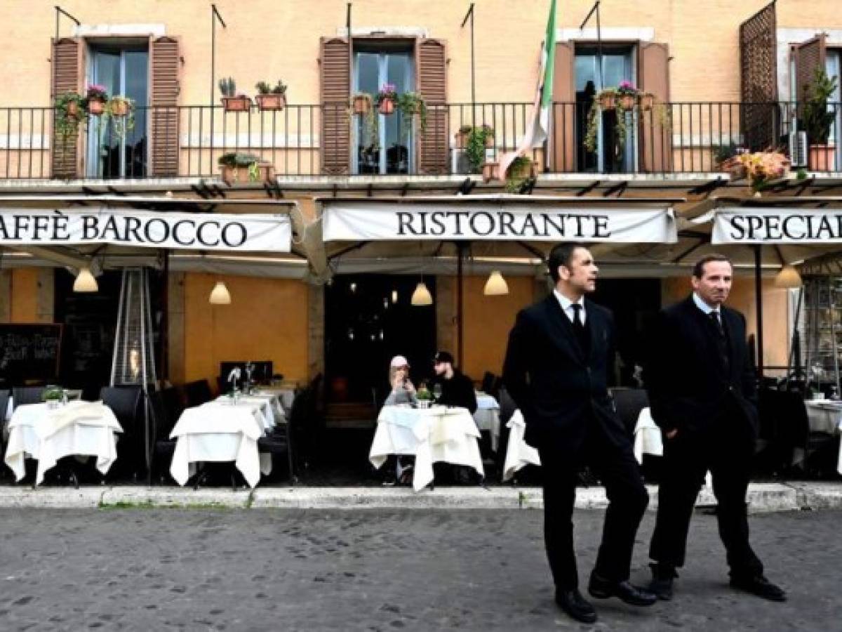 Waiters stand in front of a deserted restaurant at Piazza Navona on March 5, 2020 in Rome. - Italy closed all schools and universities until March 15 to help combat the spread of the novel coronavirus crisis. The government decision was announced moments after health officials said the death toll from COVID-19 had jumped to 107 and the number of cases had passed 3,000. (Photo by Alberto PIZZOLI / AFP)
