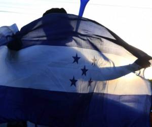 A supporter of opposition party Libertad y Refundacion (LIBRE) holds a Honduran national flag during a protest in demand of a reduction in the price of fuel in Tegucigalpa on July 27, 2018. Transport unions threaten with going again on strike if the price of fuel is not reduced. / AFP PHOTO / ORLANDO SIERRA