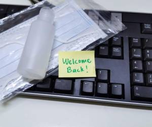 Welcome note with hand sanitizer and mask on work keyboard; Back to work note with alcohol gel to prevent coronavirus / infection