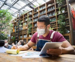 Portrait of a business manager doing the books at a restaurant wearing a facemask during the COVID-19 pandemic - reopening of business