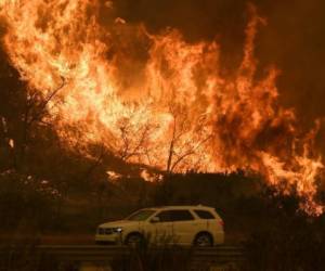 Un vehículo pasa junto a llamas en la autopista 101 cercana a la costa tras el paso del incendio Thomas, cerca de Ventura, California. AFP PHOTO / MARK RALSTON