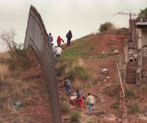 (ARCHIVO) Un grupo de presuntos emigrantes mexicanos caminan junto a la valla fronteriza separando México de Estados Unidos el 13 de febrero de 1995, del lado mexicano frente a Nogales, Arizona. La posibilidad de que el Congreso de Estados Unidos llegue a aprobar la ampliación de un muro fronterizo en hasta 1.116 km de los casi 3.200 km de límites entre ese país y México, amenaza con enturbiar las relaciones entre ambas naciones. La aprobación en diciembre por la Cámara de Representantes estadounidense de un proyecto de ley que penaliza a los migrantes indocumentados, así como a sus contratistas, y que pretende extender la valla que ya separa en algunos tramos a ambos países, ha provocado el rechazo unánime de la sociedad mexicana. AFP PHOTO CHRIS WILKINS / AFP PHOTO / CHRIS WILKINS