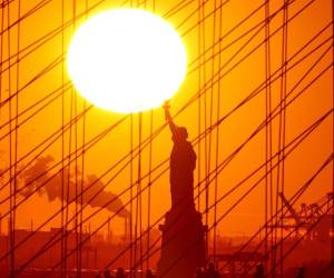 <i>El sol se pone detrás de la Estatua de la Libertad mientras la gente camina por el puente de Brooklyn en Nueva York el 6 de febrero de 2024. FOTO Charly TRIBALLEAU / AFP</i>