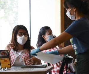 A customer is served by a waitress wearing a face mask and gloves at a Thai restaurant amid concerns over the spread of the COVID-19 coronavirus in Bangkok on March 20, 2020. (Photo by Romeo GACAD / AFP)