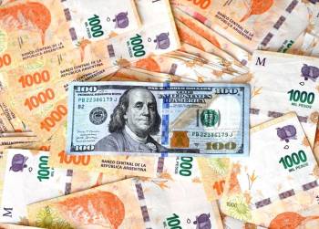 <i>Esta ilustración muestra un billete de 100 dólares encima de pesos argentinos, en Buenos Aires el 10 de octubre de 2023. FOTO LUIS ROBAYO / AFP</i>