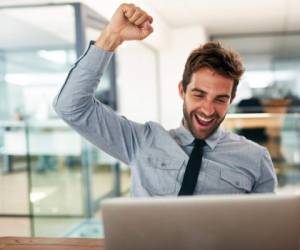 Shot of a young businessman cheering while using a laptop at his desk in an office