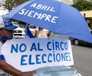 A Nicaraguan living in Costa Rica displays a placard reading 'No Circus. Election' under an umbrella reading 'Always April' during a demonstration in San Jose to commemorate the third anniversary of the beginning of the protests against the government of Nicaraguan President Daniel Ortega, on April 18, 2021. - Nicaragua's political crisis erupted in April 2018, when protests mushroomed into a popular uprising that was met with a brutal crackdown in which hundreds were killed. (Photo by Ezequiel BECERRA / AFP)