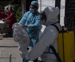 Health workers disinfect themselves while funeral workers cover with plastic the coffin of a 75-year-old man who died at the door of his home, apparently victim of COVID-19 in the La Fosa community in northern San Salvador on June 24, 2020. - The government of El Salvador inaugurated last weekend an exclusive hospital for COVID-19 patients, with the aim of decongesting other centers in the public network at a time that the disease hardly hits the country. (Photo by Yuri CORTEZ / AFP)