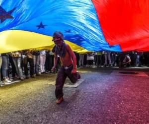 A boy runs under a Venezuelan flag during a protest of journalists and media workers against the attacks on journalists, in Caracas on June 27, 2017. / AFP PHOTO / JUAN BARRETO