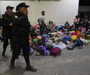 Local poli members walk by Honduran migrants heading to the United States, resting at a gas station in Zacapa, Guatemala, on October 16, 2018. - A migrant caravan set out on October 13 from the impoverished, violence-plagued country and was headed north on the long journey through Guatemala and Mexico to the US border. President Donald Trump warned Honduras he will cut millions of dollars in aid if the group of about 2,000 migrants is allowed to reach the United States. (Photo by Orlando ESTRADA / AFP)