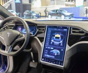 Brussels, Belgium - January 13, 2017: Luxurious interior on a Tesla Model X 90D full electric luxury crossover SUV car with a large touch screen and dashboard screen. The car is fitted with leather seats and aluminium details. The Model X uses falcon wing doors for access to the second and third row seats. The car is displayed on a motor show stand, with lights reflecting off of the body. There are people looking around and other cars on display in the background.