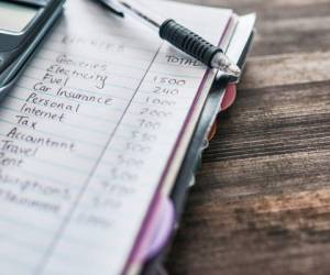 Shot of a notebook with a budget written on it and a calculator on a desk at home