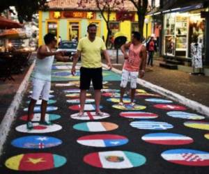 Personas posan en una calle pintada con las banderas de las selecciones que toman parte del Mundial-2014, el 11 de junio en Itu. (Foto: AFP).