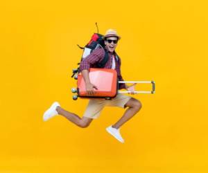 Excited happy young Asian man tourist with luggage jumping isolated on yellow studio background