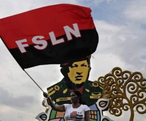 A supporter of Nicaraguan President Daniel Ortega waves a banner of his Sandinista National Liberation Front (FSLN) party, in front of an image of Venezuelan late president Hugo Chavez, during a gathering to show their support to the president as the opposition demands him to step down, in Managua on May 26, 2018.Hundreds of protesters dug in around Nicaragua on Saturday, blocking roads as at least eight more people were killed in a 24-hour period. Unrest has resumed since week-long church-mediated talks between the government and opposition to quell a month of violence broke down late on Wednesday. / AFP PHOTO / Inti OCON