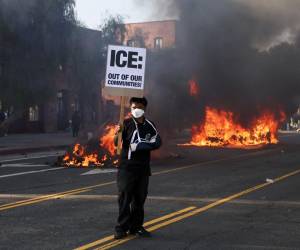 <i>Un activista sostiene un cartel mientras los se observa a automóviles incendiados durante las protestas provocadas por las redadas de inmigración en Los Ángeles, California, EE.UU., 08 de junio de 2025. EFE/ALLISON DINNER</i>