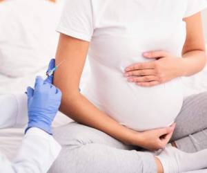 Pregnancy And Vaccination. Unrecognizable Pregnant Lady Patient Receiving Injection In Arm Sitting On Bed Indoor. Cropped