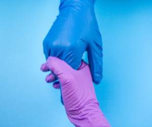 A doctor's hand saving the patient holding his hand in a glove on blue background. Concept of salvation, donorship, helping hand, coronavirus, COVID 19