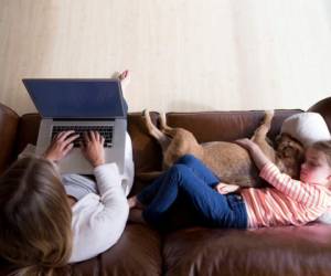 Ariel view of a woman using a laptop whilst her daughter is sleeping next to her, cuddling their pet dog.