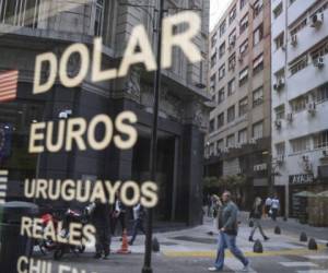 (FILES) In this file photo taken on September 26, 2018, passersby are reflected in the buy-sell board of a bureau de exchange in Buenos Aires. - The government of President Mauricio Macri on Sunday imposed foreign-exchange controls on Argentine exporters at the end of a week of financial uncertainty that saw a sharp drop in the value of the peso. Exporters were ordered to seek permission from the Central Bank of Argentina before purchasing foreign currency, according to a decree published in the Official Bulletin. (Photo by EITAN ABRAMOVICH / AFP)