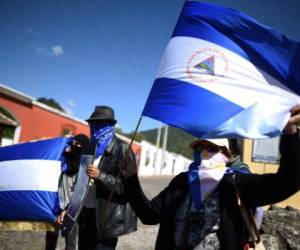 Masked Nicaraguan citizens, wave their national flag, as they demonstrate against the government of Nicaraguan President Daniel Ortega near the venue where the XXVI Ibero-American Summit is taking place in Antigua Guatemala, in Guatemala on November 16, 2018. - A group of Nicaraguans gathered near the XXVI Ibero-American Summit venue, to demand leaders to condemn repression in their country. Nicaraguan President Daniel Ortega cancelled his participation in the Summit hours before its opening. (Photo by EDWIN BERCIAN / AFP)