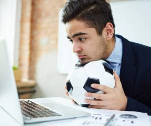 Young economist with soccer ball watching football match in front of laptop