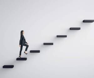 Side view of young businesswoman climbing stairs to success on concrete wall background. Leadership and career development concept