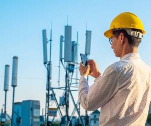 Engineer holding mobile phone testing the communications tower