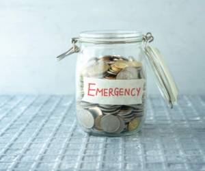Coins in glass money jar with emergency label, financial concept.