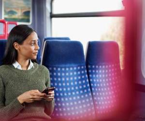 Female Passenger Sitting In Train Looking At Mobile Phone