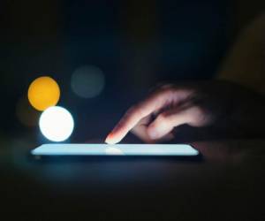 Extremely close-up shot of female finger scrolling on smartphone screen in a dark environment, with bokeh light in the background.