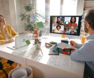 Businessman and businesswoman discussing work on video call with team members through glass partition at office