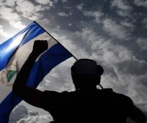 An anti-government demonstrator waves a flag while taking part in a protest in Managua, Nicaragua on June 17, 2018, demanding justice for the death of six members of a single family who died when their house was burnt at dawn on Saturday after a group of men armed wearing hoods threw a Molotov cocktail. / AFP PHOTO / MARVIN RECINOS