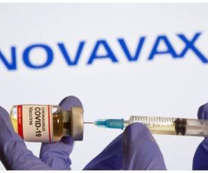 FILE PHOTO: A woman holds a small bottle labeled with a 'Coronavirus COVID-19 Vaccine' sticker and a medical syringe in front of displayed Novavax logo in this illustration taken, October 30, 2020. REUTERS/Dado Ruvic/File Photo