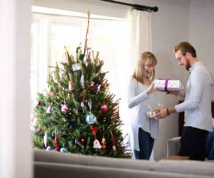 Young couple in their mid-20's and their first Christmas tree. They each hand the other a gift at the same time.