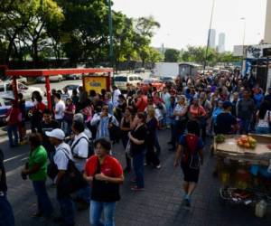 People queue at a bus stop in a street of Caracas on June 29, 2018.Venezuelan authorities offer improvised trucks -which have caused fatal accidents- as a way to palliate the transport crisis. / AFP PHOTO / Federico PARRA