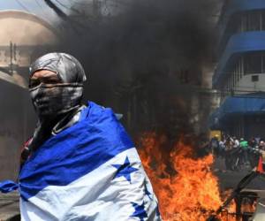 A student of the National Autonomous University of Honduras (UNAH) wrapped in a Honduran national flag is seen next to a fire that blocks a road during a protest against the approval of education and healthcare bills in the Honduran Congress in Tegucigalpa on April 29, 2019. - Honduran police dispersed with teat gas thousands of people who protested and blocked roads against education and healthcare reforms approved by the Congress. (Photo by ORLANDO SIERRA / AFP)
