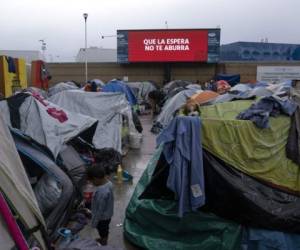 Un niño migrante se para en medio de carpas en un campamento improvisado cerca de una pantalla que dice 'Que la espera no te aburra' afuera del puerto de cruce de El Chaparral mientras él y otros esperan a que las autoridades estadounidenses les permitan iniciar su proceso migratorio en Tijuana, Baja California. estado, México, el 11 de marzo de 2021. FOTO Guillermo Arias / AFP