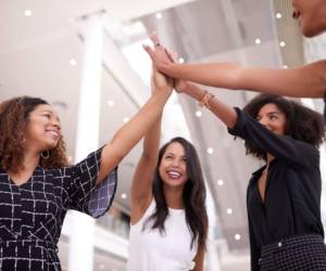 Shot of a group of young businesswomen joining hands in a modern office