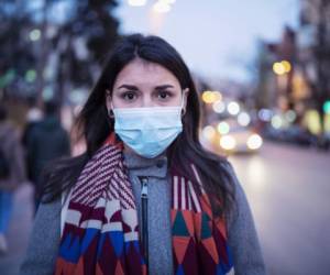 Close up portrait of Latino young woman on the street, she walking on the street with protective face mask and looking at camera, she looking sick and scared.