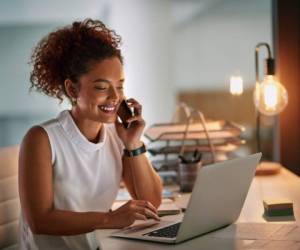 Shot of a cheerful young businesswoman taking a phone call while working late in her office