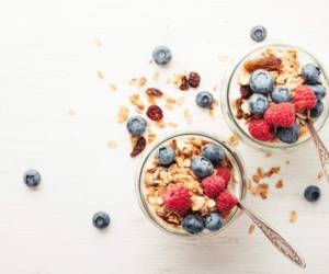 Two jars with granola, berries and yogurt on white wooden table. Top view.