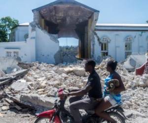People drive past the remains of the 'Sacré coeur des Cayes' church in Les Cayes on August 15, 2021, after a 7.2-magnitude earthquake struck the southwest peninsula of the country. - Hunched on benches, curled up in chairs or even lying the floor, those injured in the powerful earthquake that wreaked havoc on Haiti on Saturday crowded an overburdened hospital near the epicenter. The emergency room in Les Cayes, in southwestern Haiti, which was devastated by the 7.2-magnitude quake on Saturday morning that killed at least 724 people, is expecting reinforcements to help treat some of the thousands of injured. (Photo by Reginald LOUISSAINT JR / AFP)
