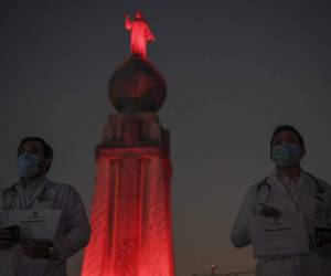 El personal médico se para frente al monumento al Divino Salvador del Mundo, que se ilumina en rojo como tributo al trabajo que realizan durante la pandemia del nuevo coronavirus. Foto por Yuri CORTEZ / AFP