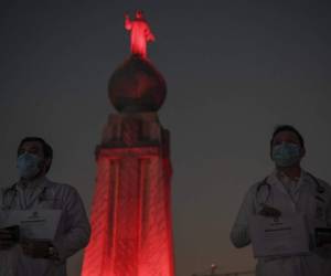 El personal médico se para frente al monumento al Divino Salvador del Mundo, que se ilumina en rojo como tributo al trabajo que realizan durante la pandemia del nuevo coronavirus. Foto por Yuri CORTEZ / AFP