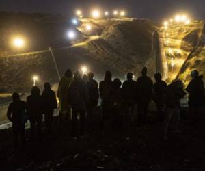 Central American migrants stand on a mound before attempting to cross from Tijuana to San Diego in the US on New Year's Eve, as seen from Tijuana, Baja California state, Mexico on December 31, 2018. - Around 100 Central American migrants made a failed attempt on New Year's Eve to cross over from Mexico into the United States. As night fell and people on both sides of the frontier prepared to celebrate New Year's Eve, the migrants tried to cross over but at least two smoke bombs were hurled and they ultimately held back. (Photo by Guillermo Arias / AFP)