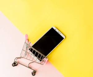 Blank screen white cellphone and shopping carts on pastel pink and yellow background. Minimal style, flatlay.