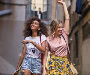 Two multi-ethnic young women friends having fun sharing music in the street.