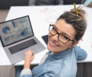 Creative woman working online at a co-working space using a laptop computer and looking at the camera smiling **DESIGN ON SCREEN IS OUR OWN**